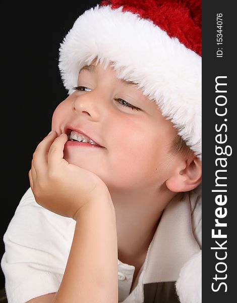 Cute young boy wearing a christmas hat against a black background. Cute young boy wearing a christmas hat against a black background