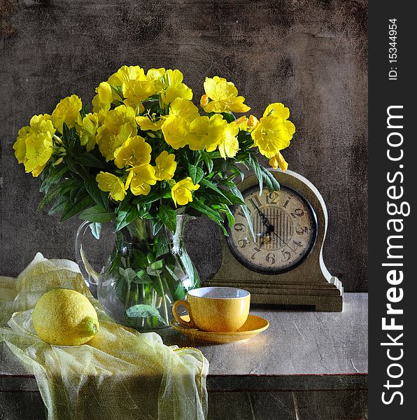 on a table a vase stands with yellow, alongside yellow cup with a saucer, clock, lemon and fabric. on a table a vase stands with yellow, alongside yellow cup with a saucer, clock, lemon and fabric