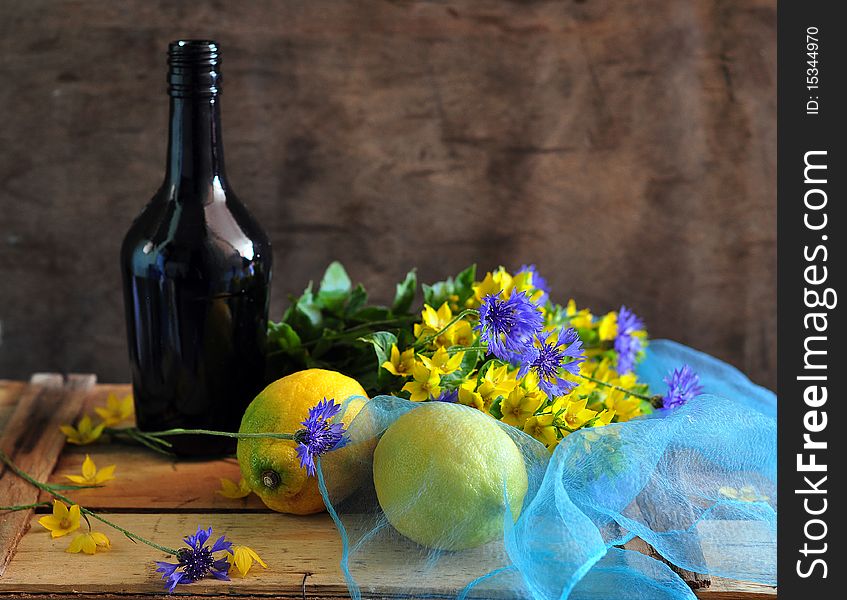 a bottle stands on a box, two lemons and flowers lie alongside. a bottle stands on a box, two lemons and flowers lie alongside