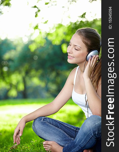 A young girl listens to music with headphones in the park. A young girl listens to music with headphones in the park