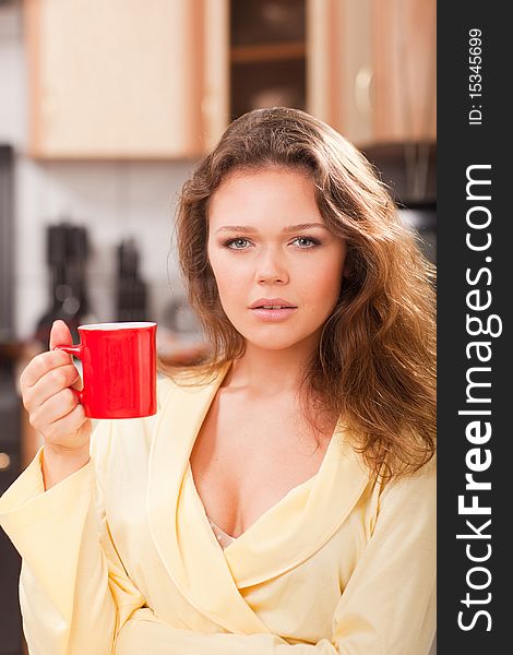 Attractive young adult with red cup of tea in the kitchen. Attractive young adult with red cup of tea in the kitchen