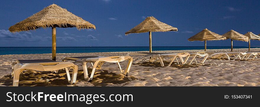 Panorama of empty sunbeds with umbrellas at night on the beach of Sal, Cabo Verde, Cape Verde. Panorama of empty sunbeds with umbrellas at night on the beach of Sal, Cabo Verde, Cape Verde