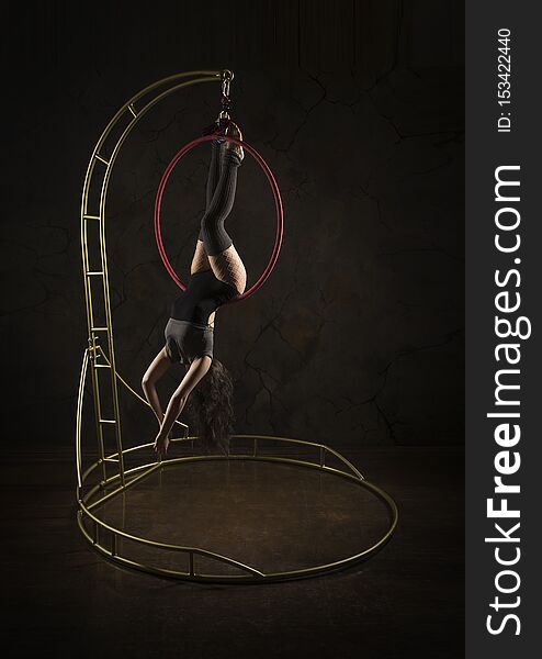 Gorgeous girl, aerial acrobat, in a dark suit performs acrobatic elements on a portable air ring, in the stage light
