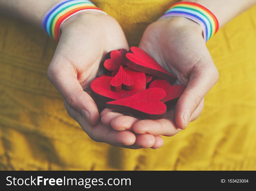 Hands with rainbow LGBT ribbon wristband holding heap of wooden red hearts