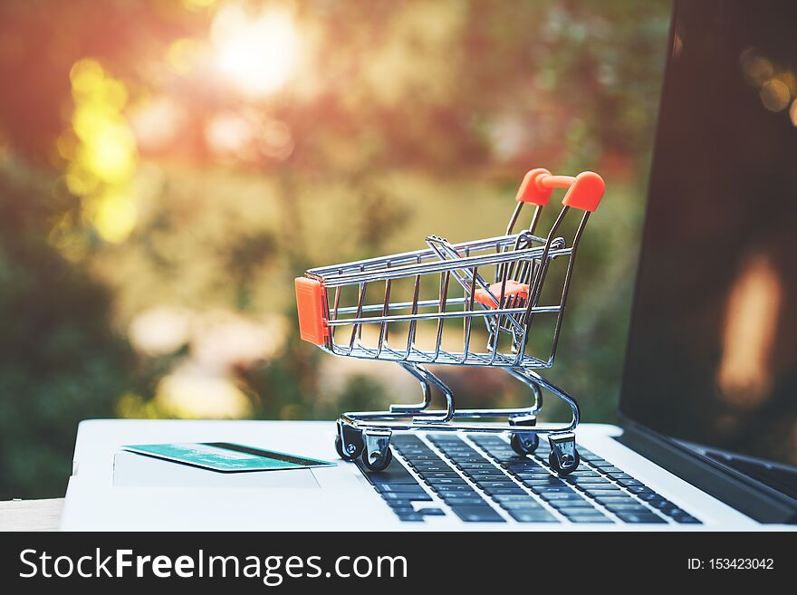 Mini toy trolley, credit card and open laptop on wooden table, copy space, online shopping concept