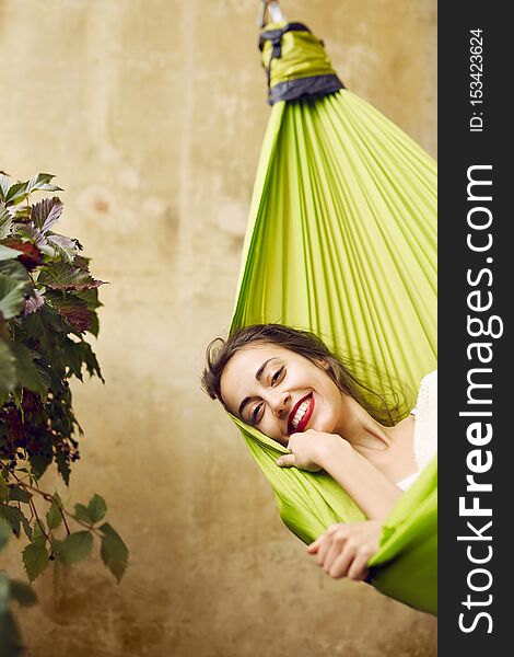 Portrait of smiling young woman relaxing in a hammock on the terrace house. Woman lying and covered with plaid in a hammock. Concept of rest, enjoyment, carefree.