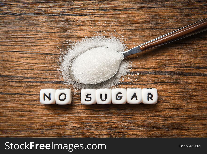 No sugar text blocks with white sugar on spoon wooden background / suggesting dieting and eat less sugar for health concept