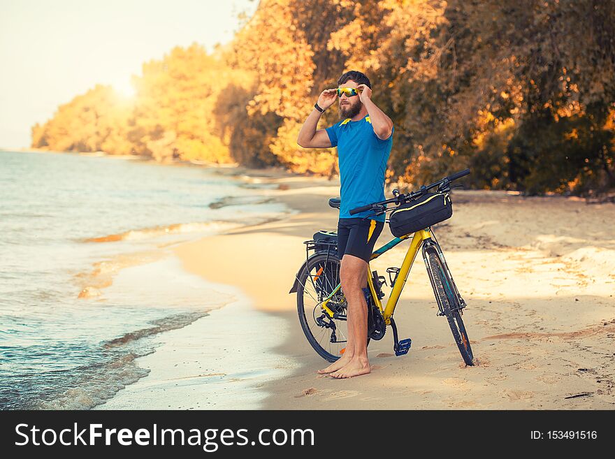 Bearded Man Cyclist Rides Along The Sandy Beach On A Mountain Bike.