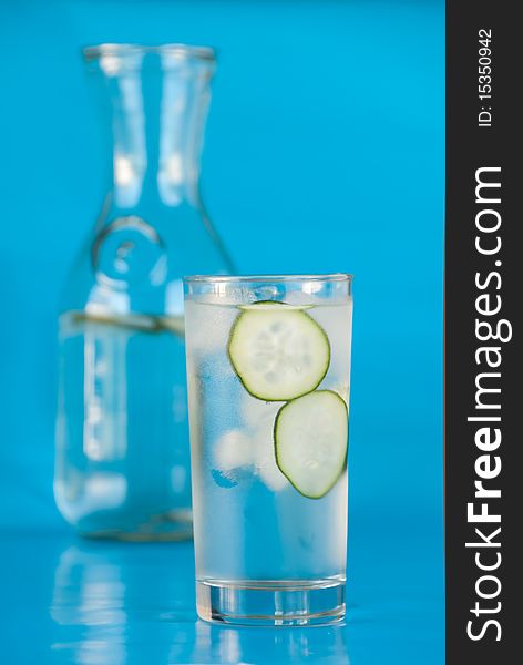 Ice water with cucumbers on blue in front of glass carafe. Ice water with cucumbers on blue in front of glass carafe