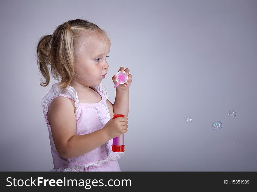 Blonde little girl trying to make small soap bubbles