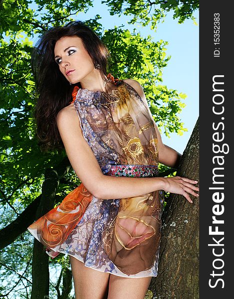 Fashion shoot of a young brunette girl in a light brown dress. The image is taken outdoors, on a nature background with trees. Fashion shoot of a young brunette girl in a light brown dress. The image is taken outdoors, on a nature background with trees.