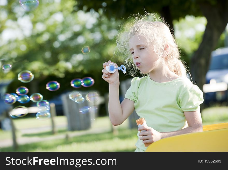 Cute little girl making soap bubbles in a park