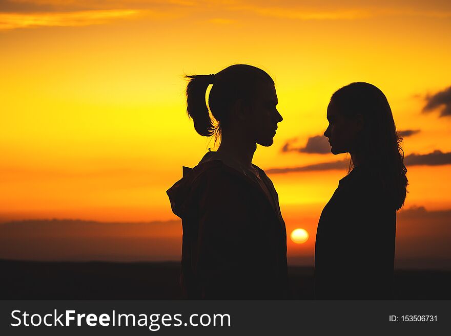 Waist silhouettes of a young millenial couple in love with a man and a girl look at each other. Two profile of a young couple at sunset.