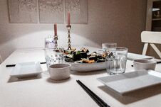 Plates And Dishes On The Table In An Apartment. Self Made Sushi Roll. Romantic Dinner With Ambient Light From Candle Stock Photos