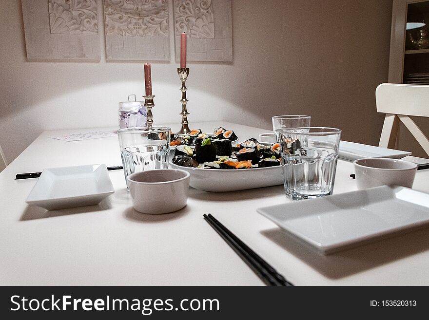 Plates and Dishes on the table in an apartment. self made Sushi roll. Romantic dinner with ambient light from candle