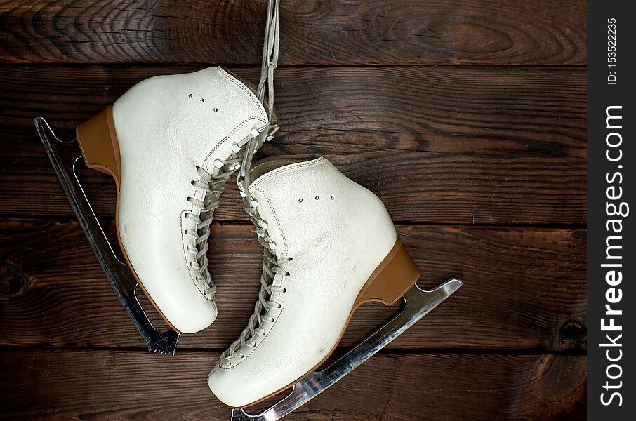 white leather womens skates for figure skating hang on a nail, brown wooden background