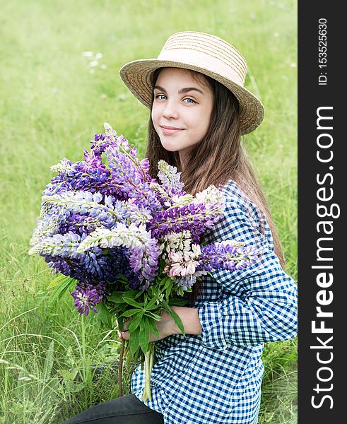 Girl in a summer field with a straw hat and a bouquet of lupins