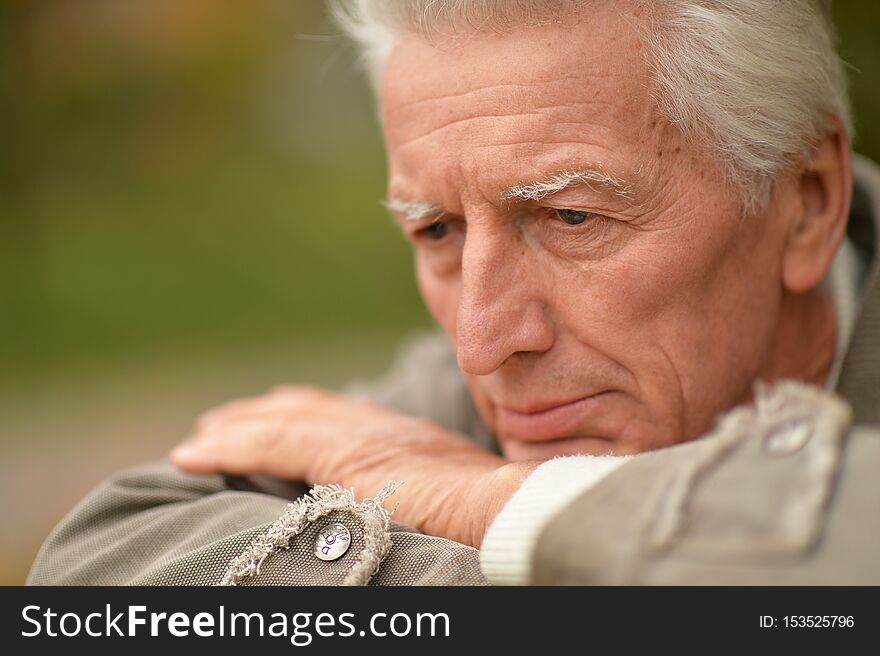 Portrait of sad senior man posing in autumn park