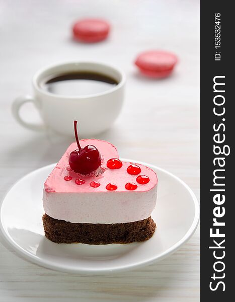 Souffle cake in the form of heart with cup of coffe and macaroons on wooden table