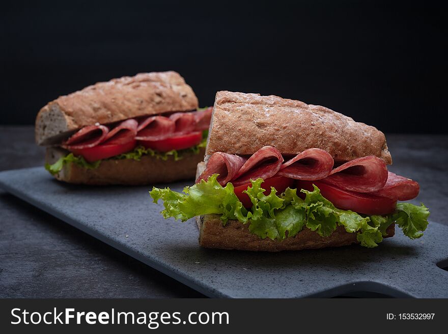 Breakfast sandwiches with salami, tomato, lettuce on gray board as background. Breakfast sandwiches with salami, tomato, lettuce on gray board as background