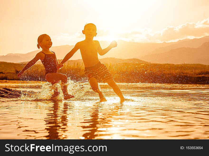 Portrait of two children aged 3 and 6 playing in the sea and spraying water around them