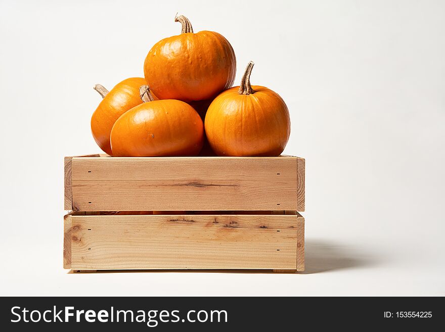 Ripe orange pumpkins in a wooden box on white background