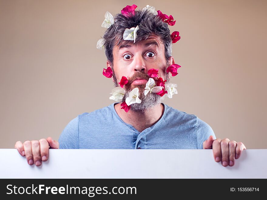 Handsome surprised man with flowers on beard and hair. People, emotions, summer or spring concept