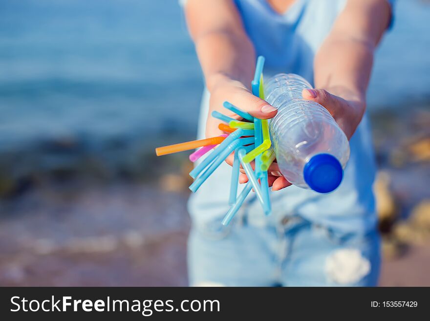 Woman Holds Plastic Bottle And Straws In Hands On The Beach. Beat Plastic Pollution Concept