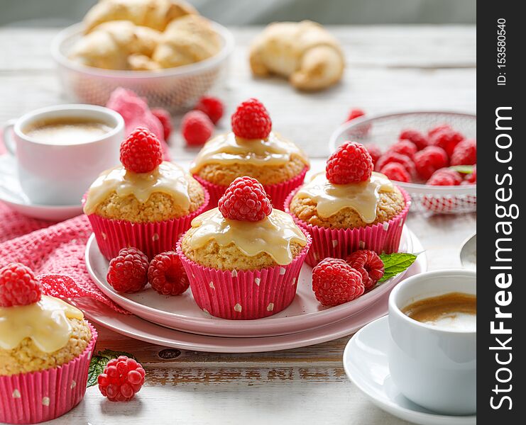 Cupcakes with white chocolate and fresh raspberries on a ceramic plate on a wooden white table, close up. A delicious dessert or breakfast.