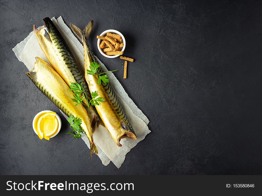 Smoked fish mackerel or scomber on a white parchment paper. Black or dark stone background. Top view. Smoked fish mackerel or scomber on a white parchment paper. Black or dark stone background. Top view