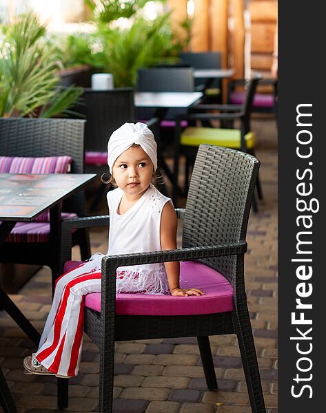 Stylish little girl with white turban on her head sitting in a cafe