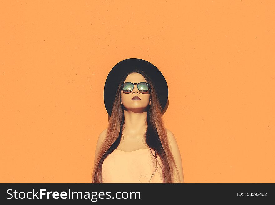 Fashionable girl standing wearing fashionable sunglasses and black hat with a solid color as background