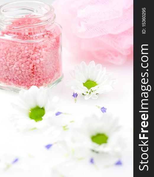 Pink bath salt and a sponge on a table with daisy in front. Pink bath salt and a sponge on a table with daisy in front