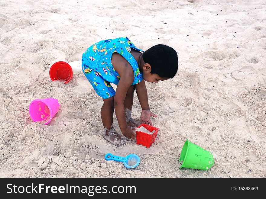 An handsome Indian kid playing with sand at a tropical beach