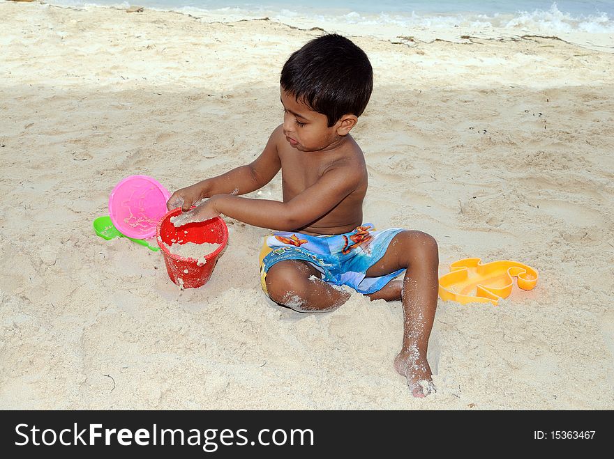 An handsome Indian kid playing with sand at a tropical beach