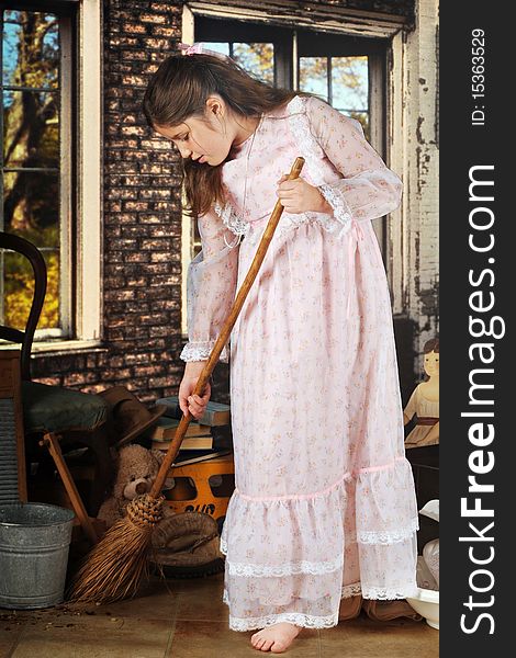 An attractive preteen in an old-fashioned dress, sweeping with an old-fashioned broom in great-grandma's brck shed filled with her old stuff. An attractive preteen in an old-fashioned dress, sweeping with an old-fashioned broom in great-grandma's brck shed filled with her old stuff.