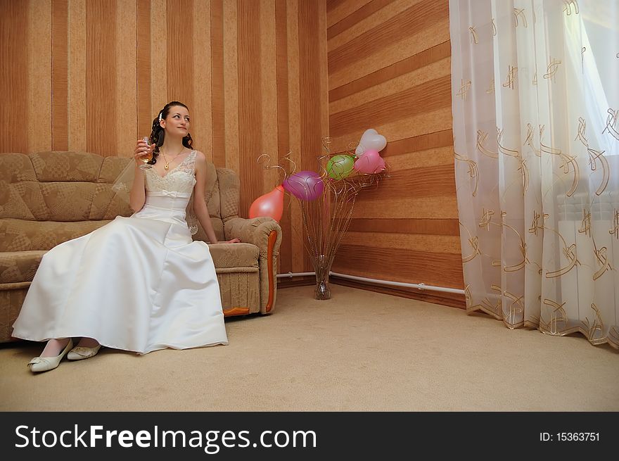 The bride sits on a sofa, drinks a drink and looks at the window. The bride sits on a sofa, drinks a drink and looks at the window