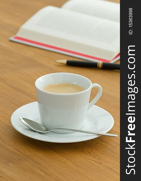 White coffee cup with open book and pen on a wooden table. White coffee cup with open book and pen on a wooden table