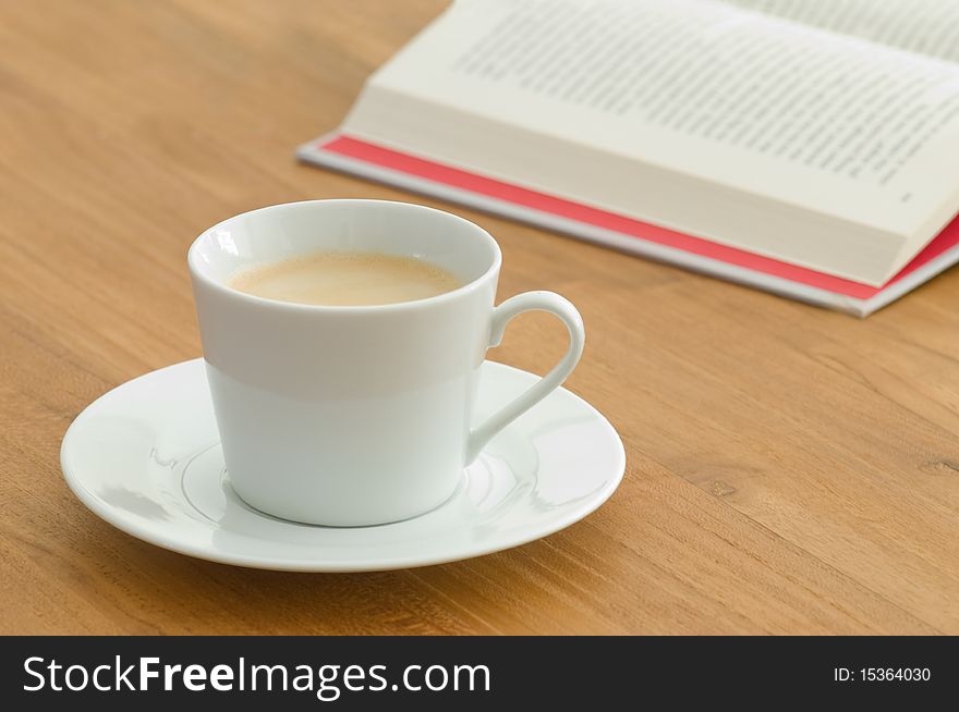 White coffee cup with open book on a wooden table. White coffee cup with open book on a wooden table