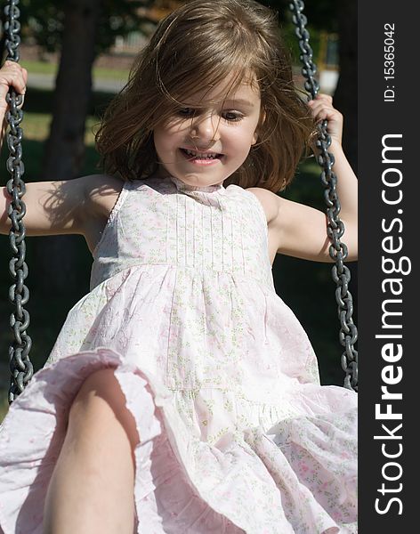 Close-up of a cheerful little girl swinging, looking away from the camera. Close-up of a cheerful little girl swinging, looking away from the camera