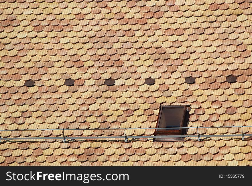 Lots of brown tiles and a window on a roof. Lots of brown tiles and a window on a roof