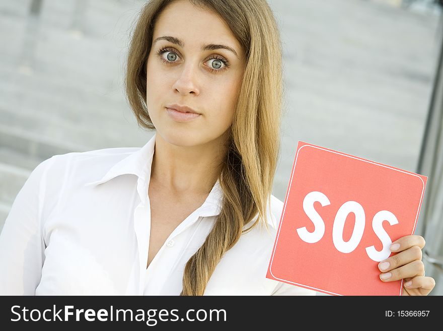 Business woman on a background of office space in the hands holding a red card with the text of SOS. Prayer in aid. Business woman on a background of office space in the hands holding a red card with the text of SOS. Prayer in aid