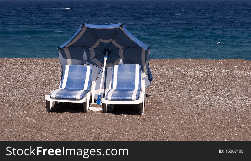 Blue and white chairs and umbrella on the beach close to the rough sea. Blue and white chairs and umbrella on the beach close to the rough sea.