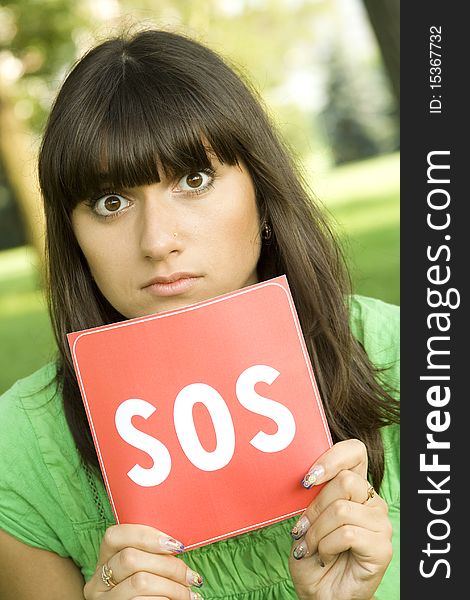 Young woman outdoors in the park holding a red card with the text of SOS. Prayer in aid. Young woman outdoors in the park holding a red card with the text of SOS. Prayer in aid
