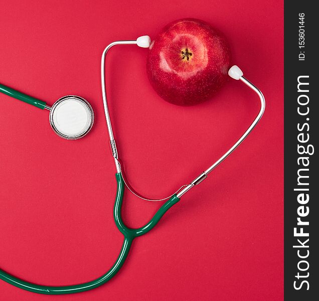 Ripe apple and green medical stethoscope on red background, health care concept