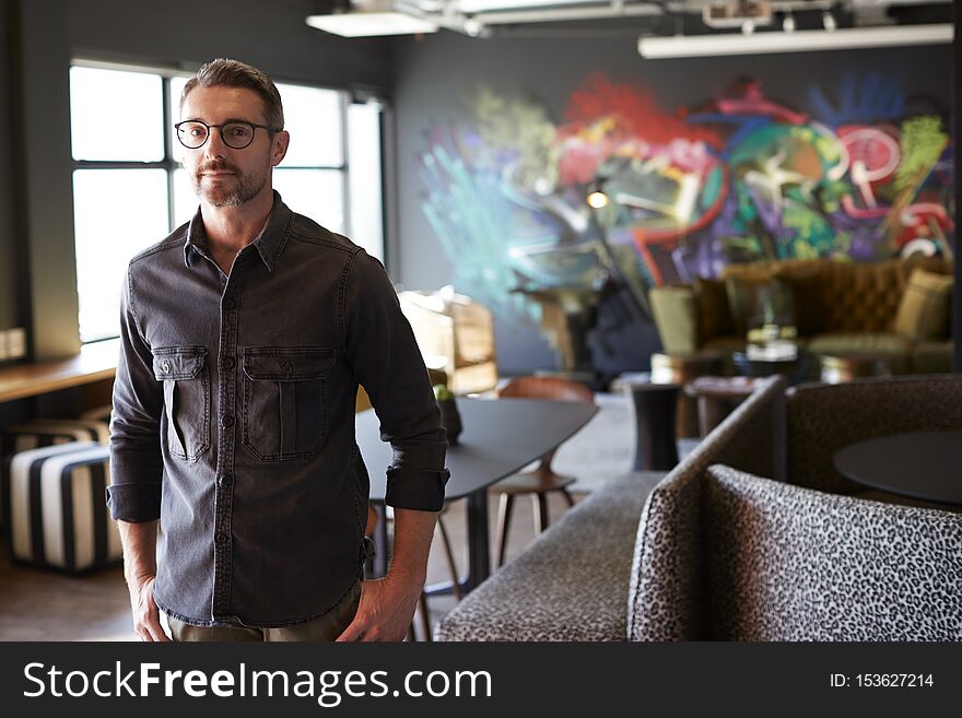 Middle aged white male creative standing in casual office canteen, cafe area looking to camera