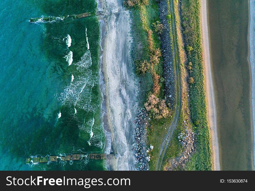 An overhead shot of a narrow shore in the middle of the sea with pathway and greenery on it