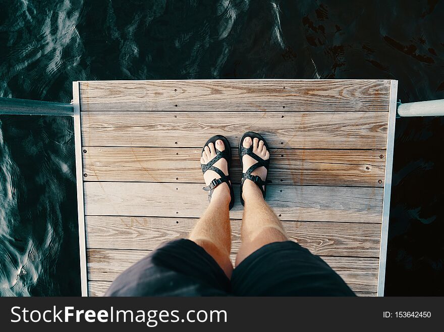 The feet of a male standing on a wooden surface over the body of water