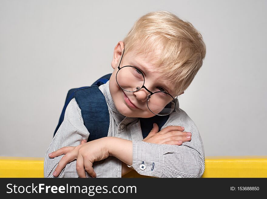 Portrait of a blond smiling boy in glasses and with a school backpack on a white background. School concept