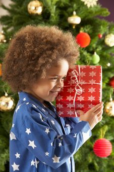 Boy Holding Gift In Front Of Christmas Tree Stock Image